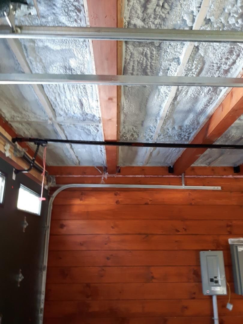 Plafond de garage orange avec poutres en bois et toiture texturée et isolée. Barre de support noire et composants électriques visibles.