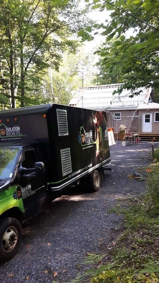 Un camion noir est garé devant une maison dans une zone boisée. Des travaux de toiture sont visibles.