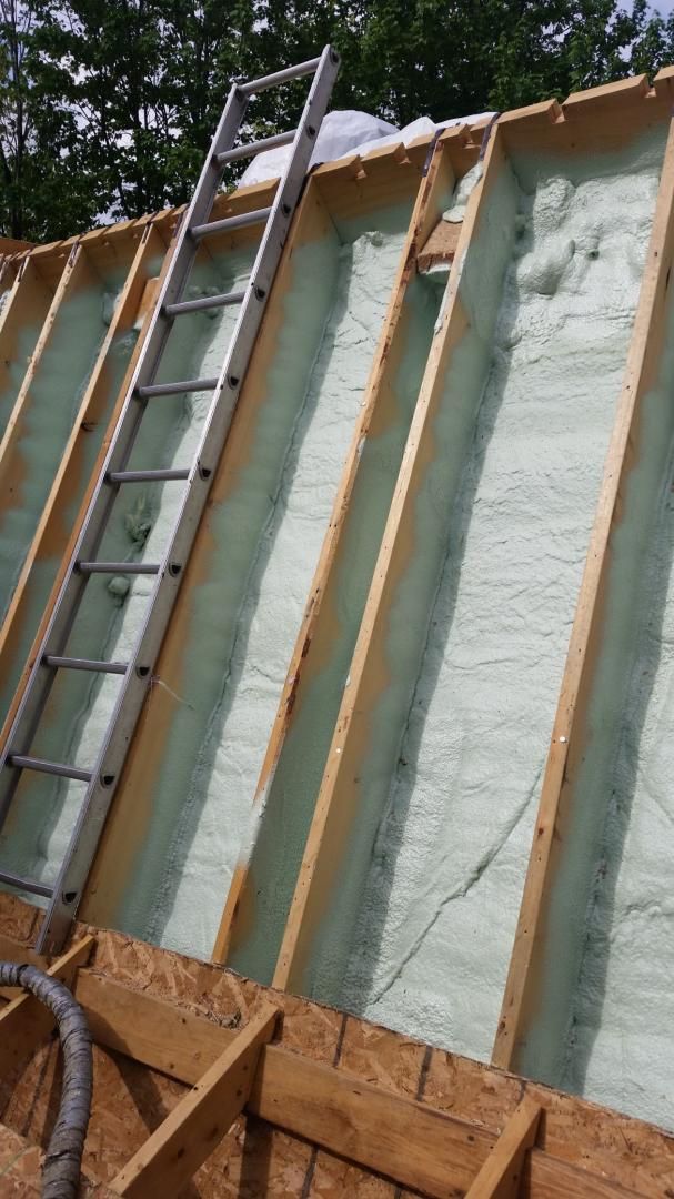 Un toit en construction avec une isolation en mousse pulvérisée, une échelle s'appuie contre les chevrons.