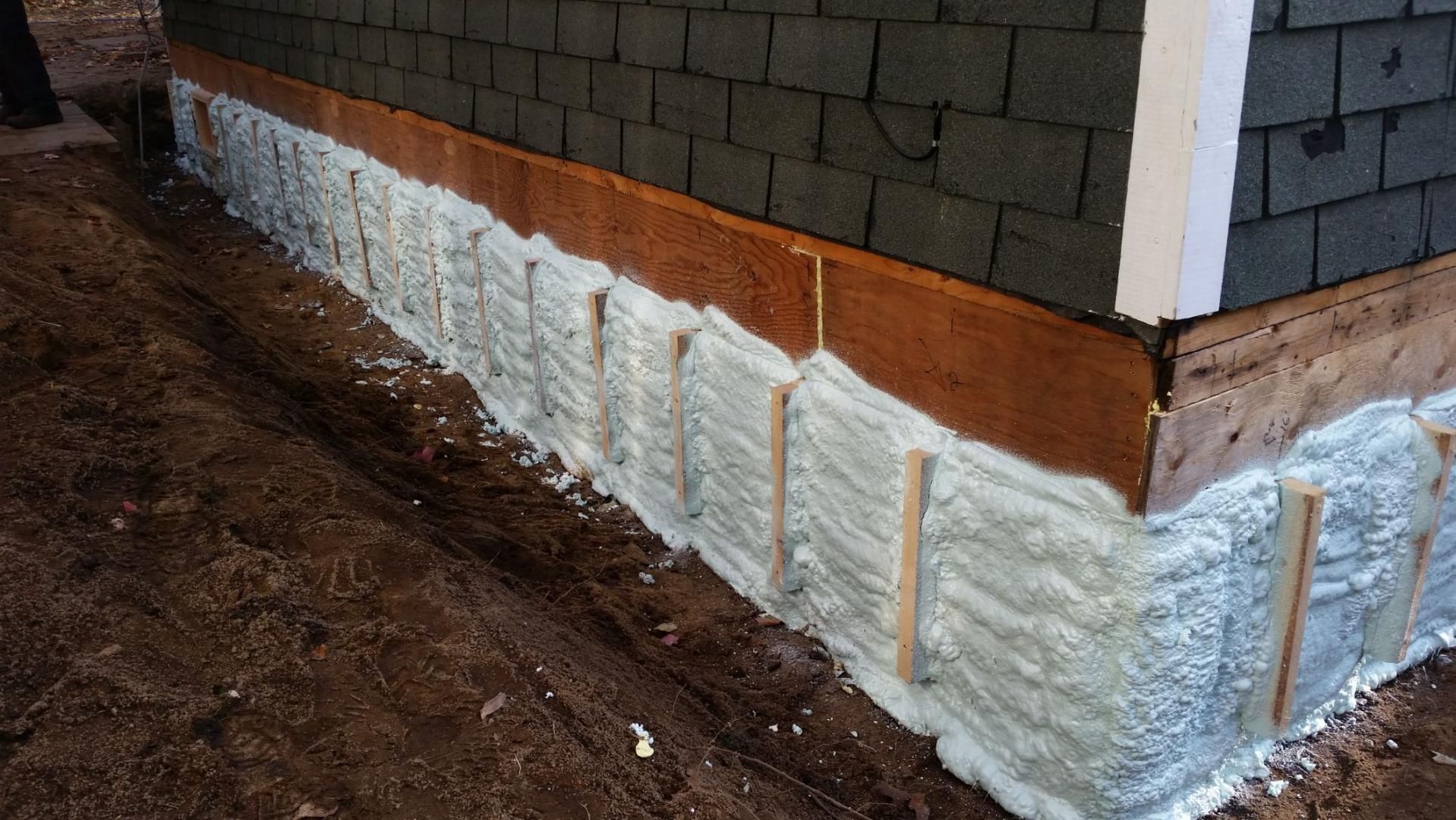 Isolation des fondations avec mousse projetée. Revêtement brun, moulures blanches, sol en terre battue.