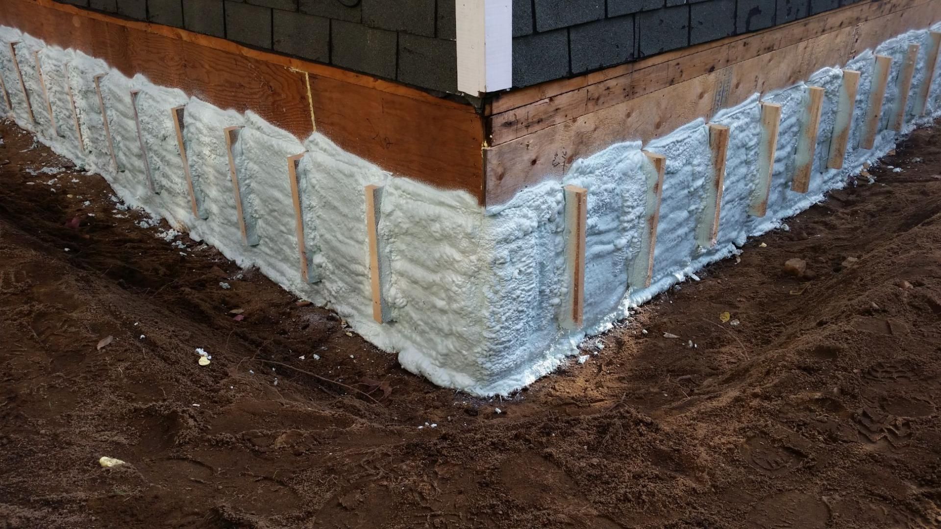 Coin d'une fondation de bâtiment avec mousse isolante et bandes de bois, sur sol brun.