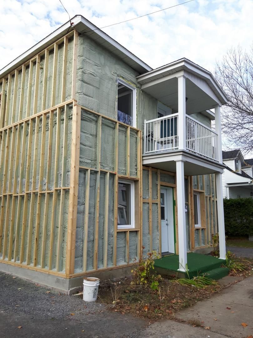 Extérieur d'une maison à deux étages en rénovation; ossature bois fixée sur le côté avec isolation visible.