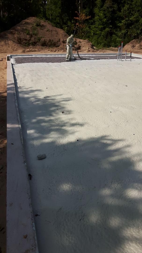 Fondation en béton fraîchement coulée avec coffrages visibles ; un ouvrier est près du centre.