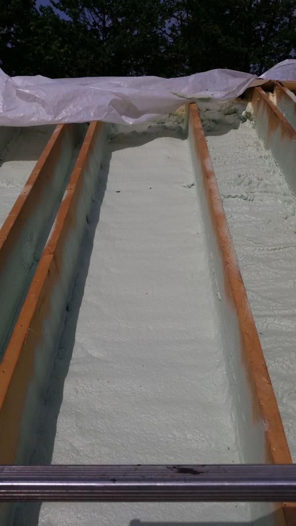Isolation en mousse appliquée entre des poutres en bois, recouverte d'une bâche en plastique ; vue extérieure.