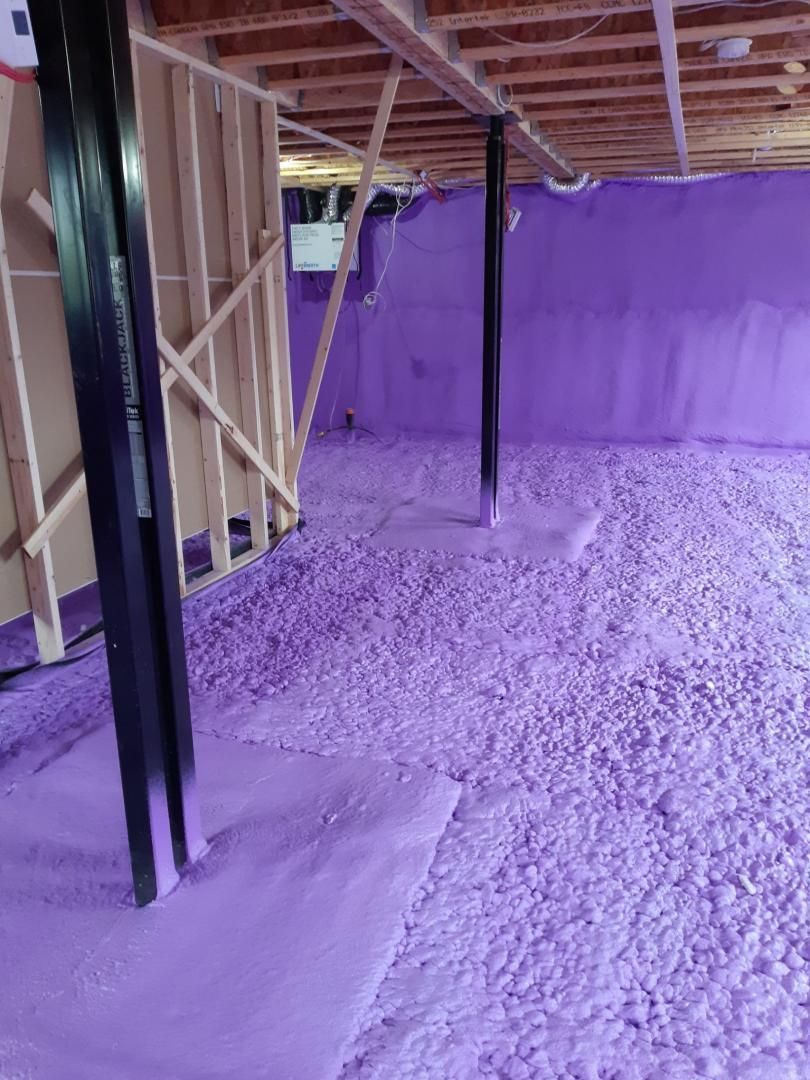 Isolation violette dans un sous-sol en construction, autour des poutres de soutien et des murs non finis.