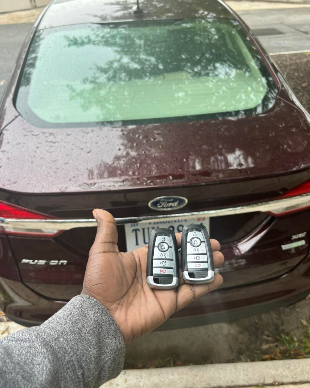 A person is holding two keys in front of a ford car.