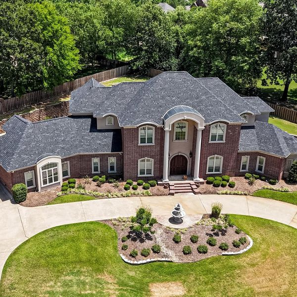 An aerial view of a large brick house with a gray roof surrounded by trees.