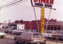 A car is parked in front of a diner dining room sign.