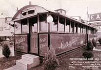 A black and white photo of a trolley parked in front of a building.