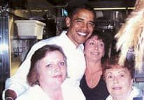 Barack obama is posing for a picture with three women in a kitchen.
