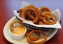 A basket of onion rings with dipping sauce on a plate.
