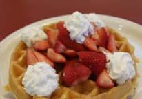 A waffle with strawberries and whipped cream on a plate.