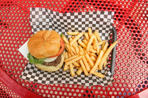 A hamburger and french fries on a checkered paper on a red table.