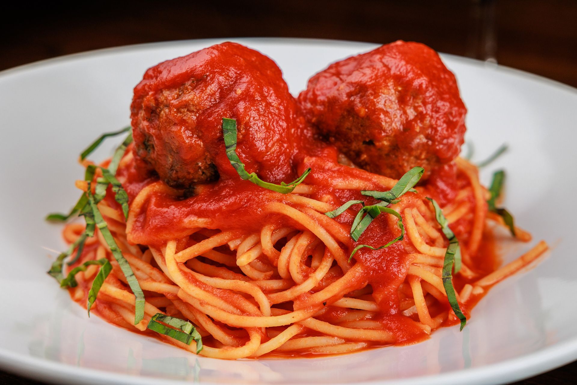 A white plate topped with spaghetti and meatballs in tomato sauce.