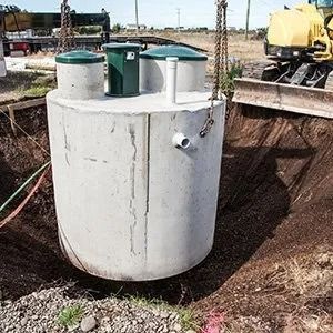 A large concrete septic tank suspended by chains over an excavation pit at a construction site.