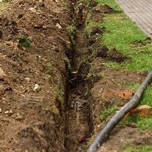 A narrow, deep trench dug into the earth next to a grassy lawn and a paved walkway.