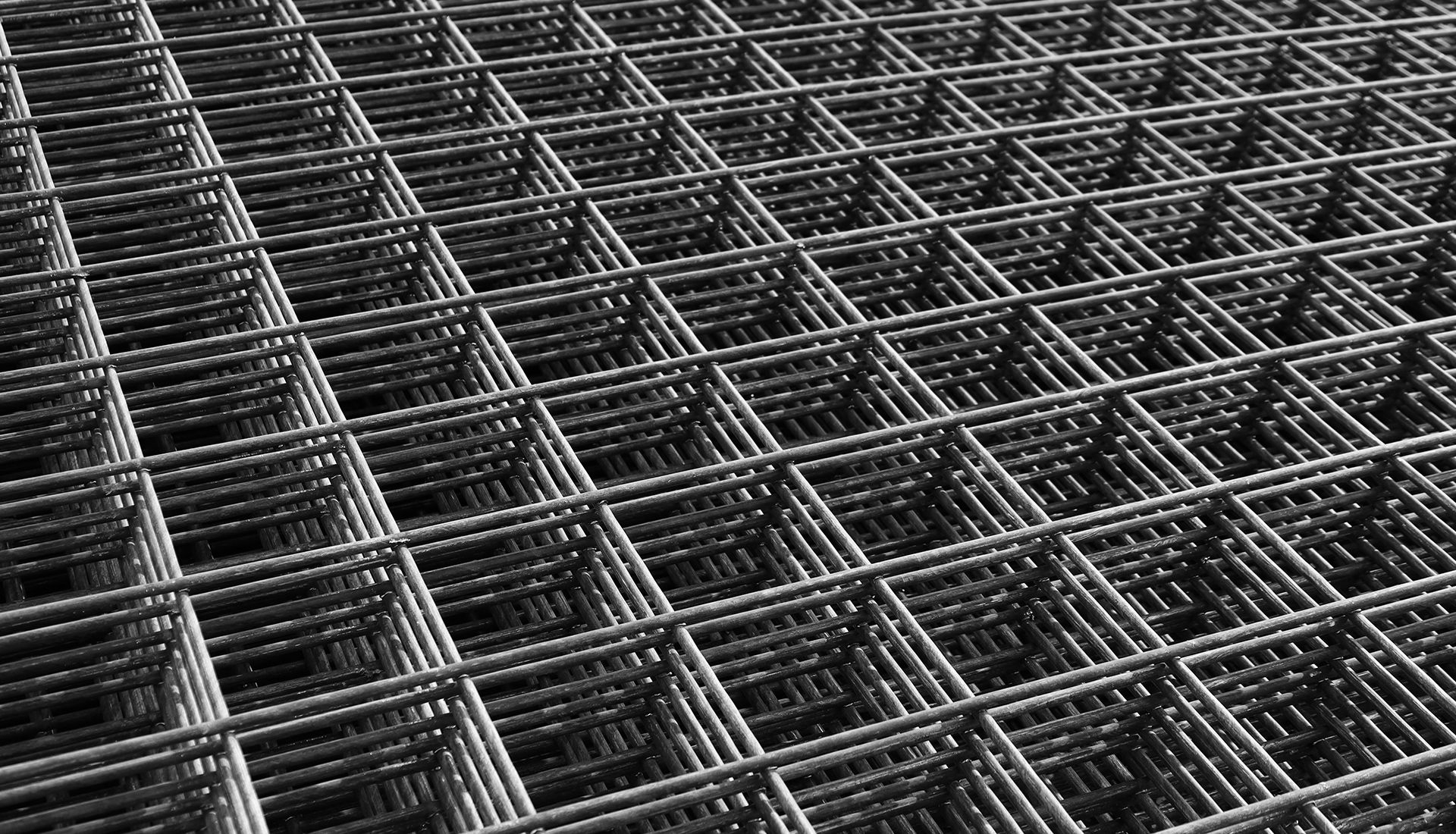 A close-up, high-angle view of a dark gray steel wire mesh grid used for concrete reinforcement.