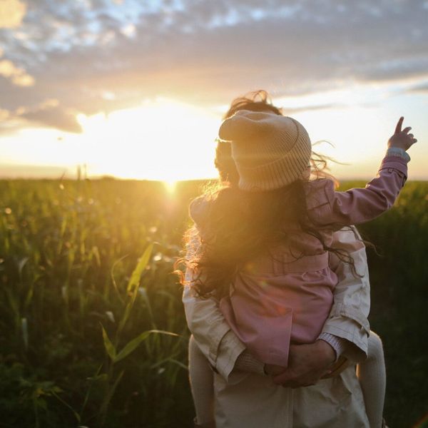 A woman is carrying a little girl on her shoulders in a field at sunset.