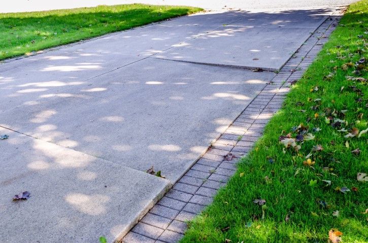 Uneven concrete driveway with raised section, bordered by grass and a brick edge.