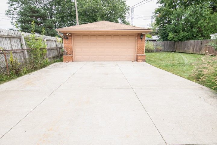 Concrete driveway leading to a tan brick garage with closed door; flanked by wooden fences and grass.
