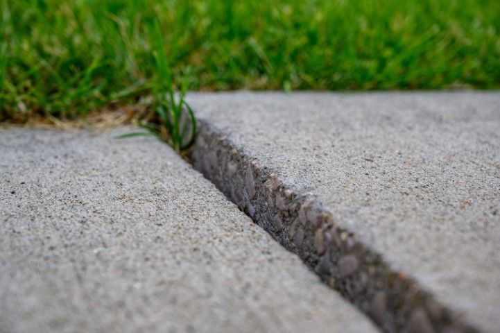 Close-up of a concrete sidewalk with a deep crack, green grass in the background.