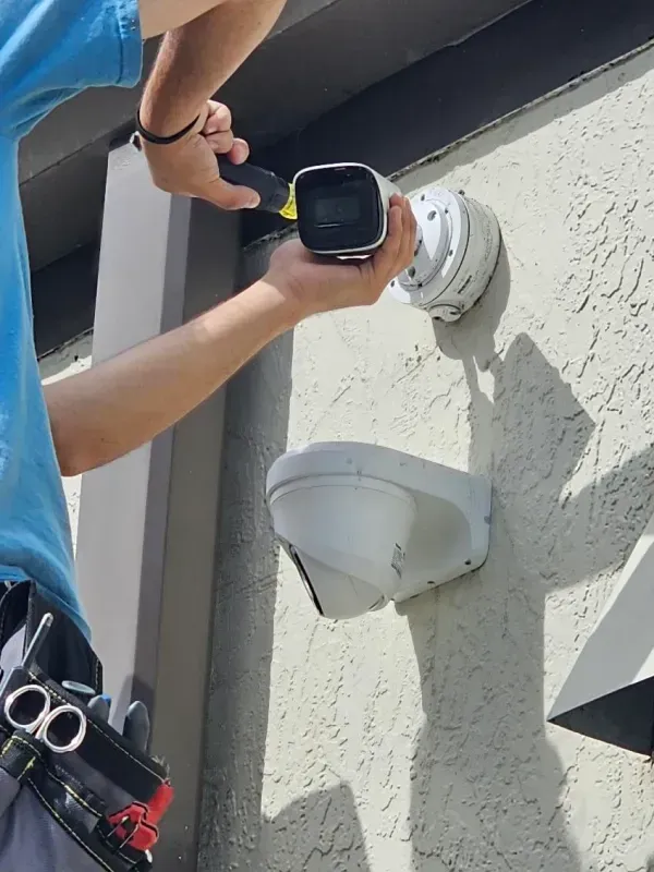 Person installs a security camera on a stucco wall. A second camera is mounted below.
