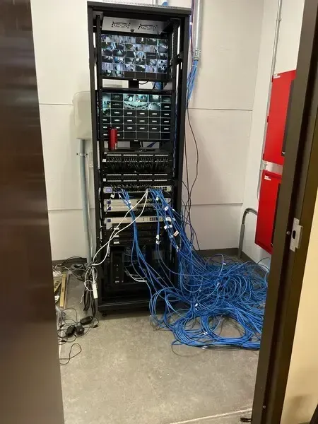 A server rack in a room with blue network cables strewn on the floor. A red fire safety box is visible.
