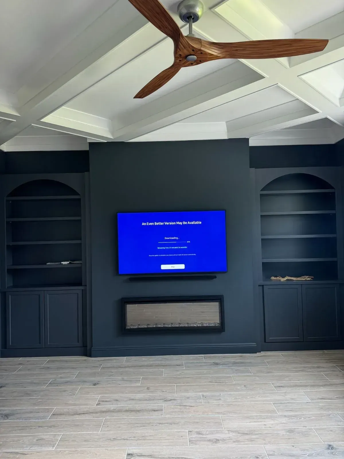Dark blue entertainment center with TV, fireplace, and built-in bookshelves. Ceiling fan and white crossbeams.