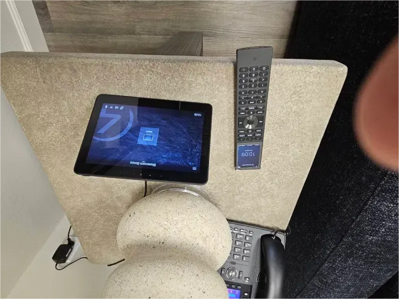 Tablet and remote on a beige table; lower section of a vase. A hand appears on the right.