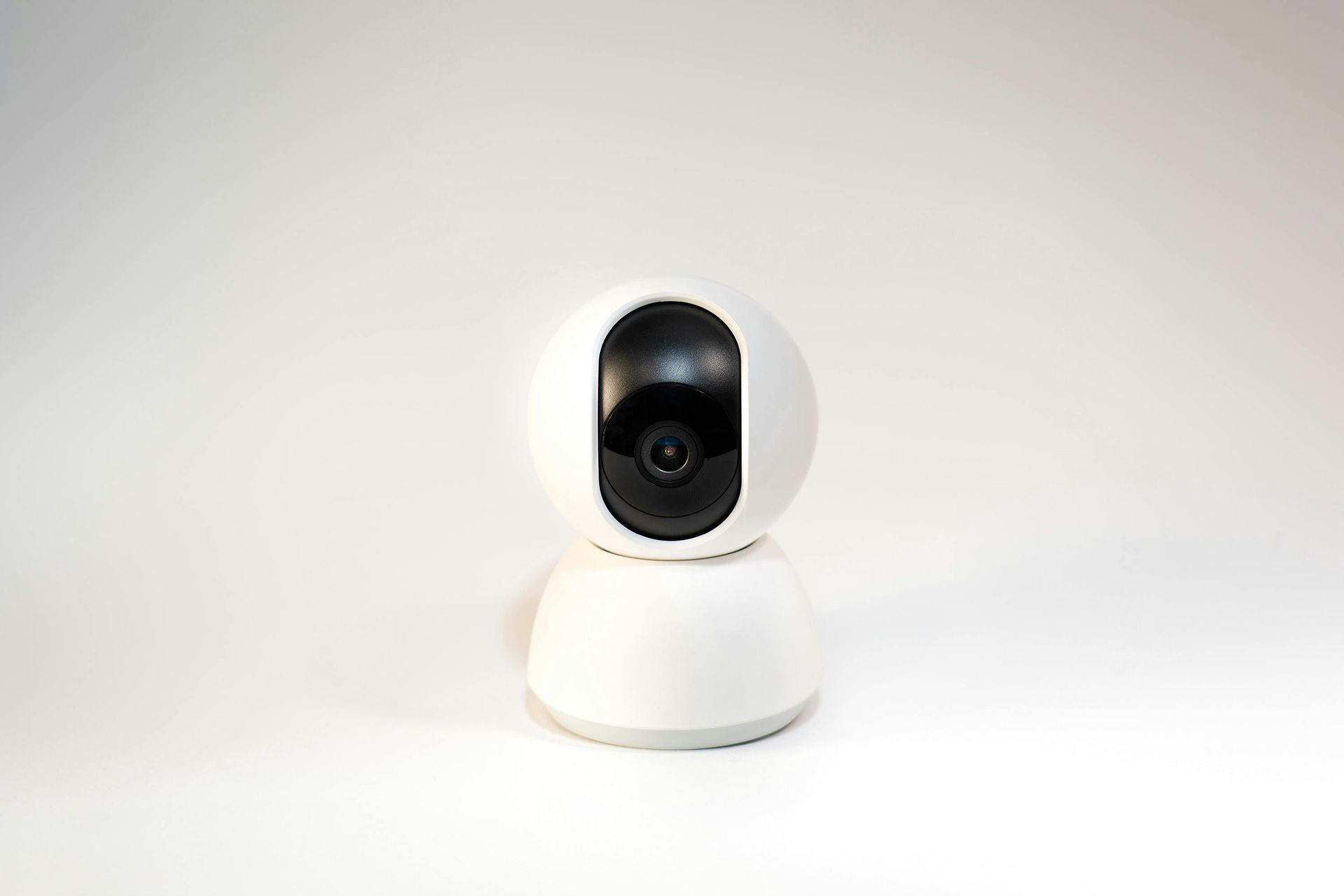 White security camera on a white background, with a black lens.