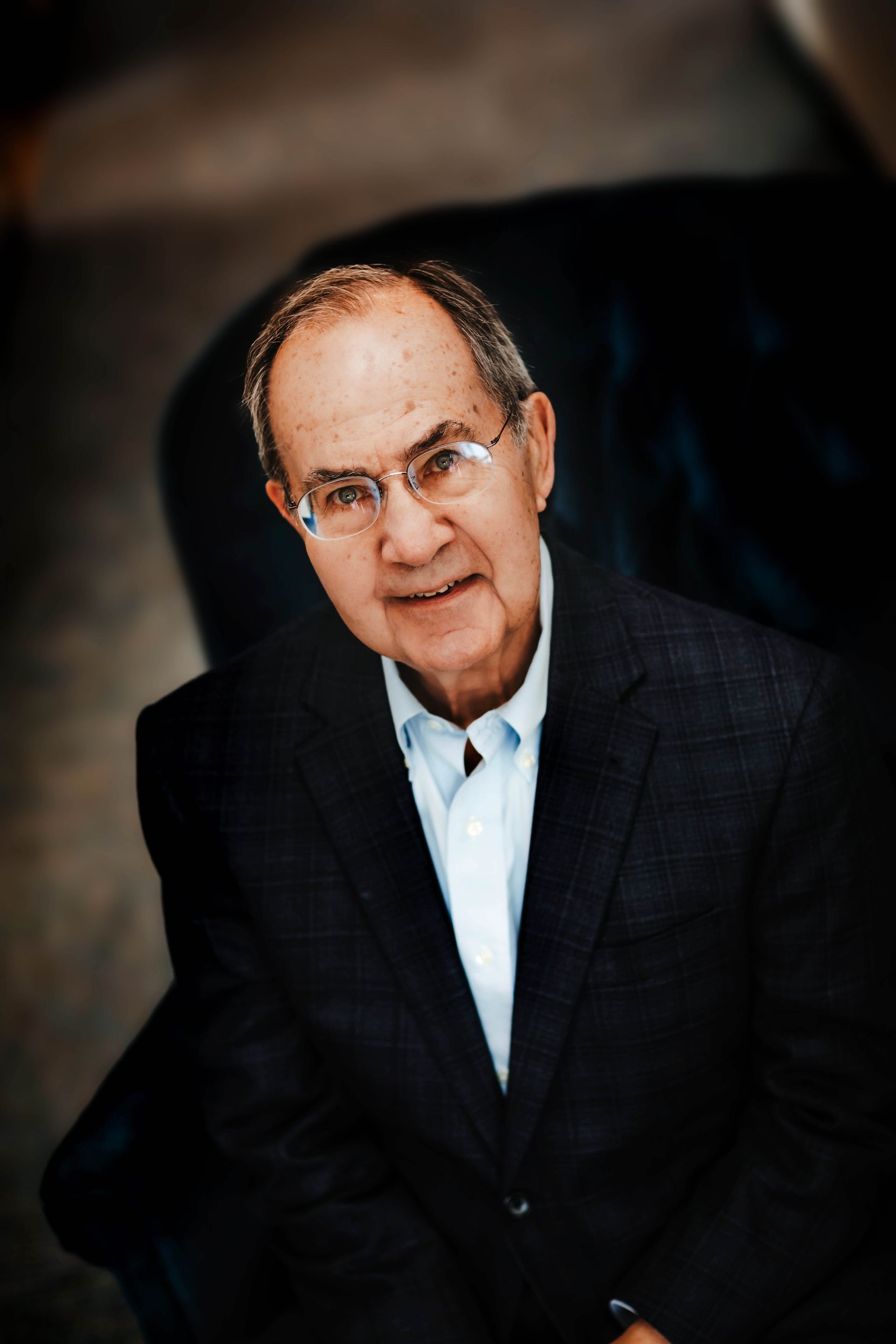 A man in a suit and glasses is sitting in a chair.