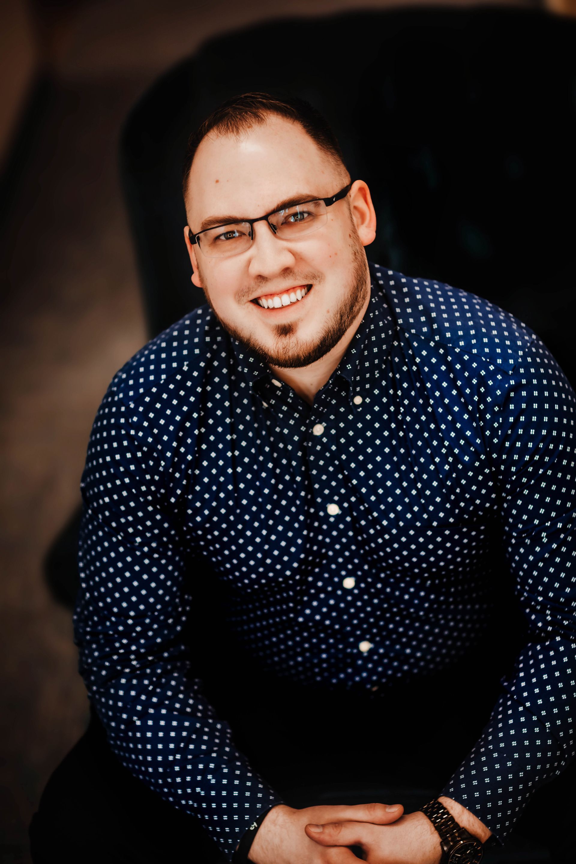 A man wearing glasses and a blue polka dot shirt is smiling for the camera.