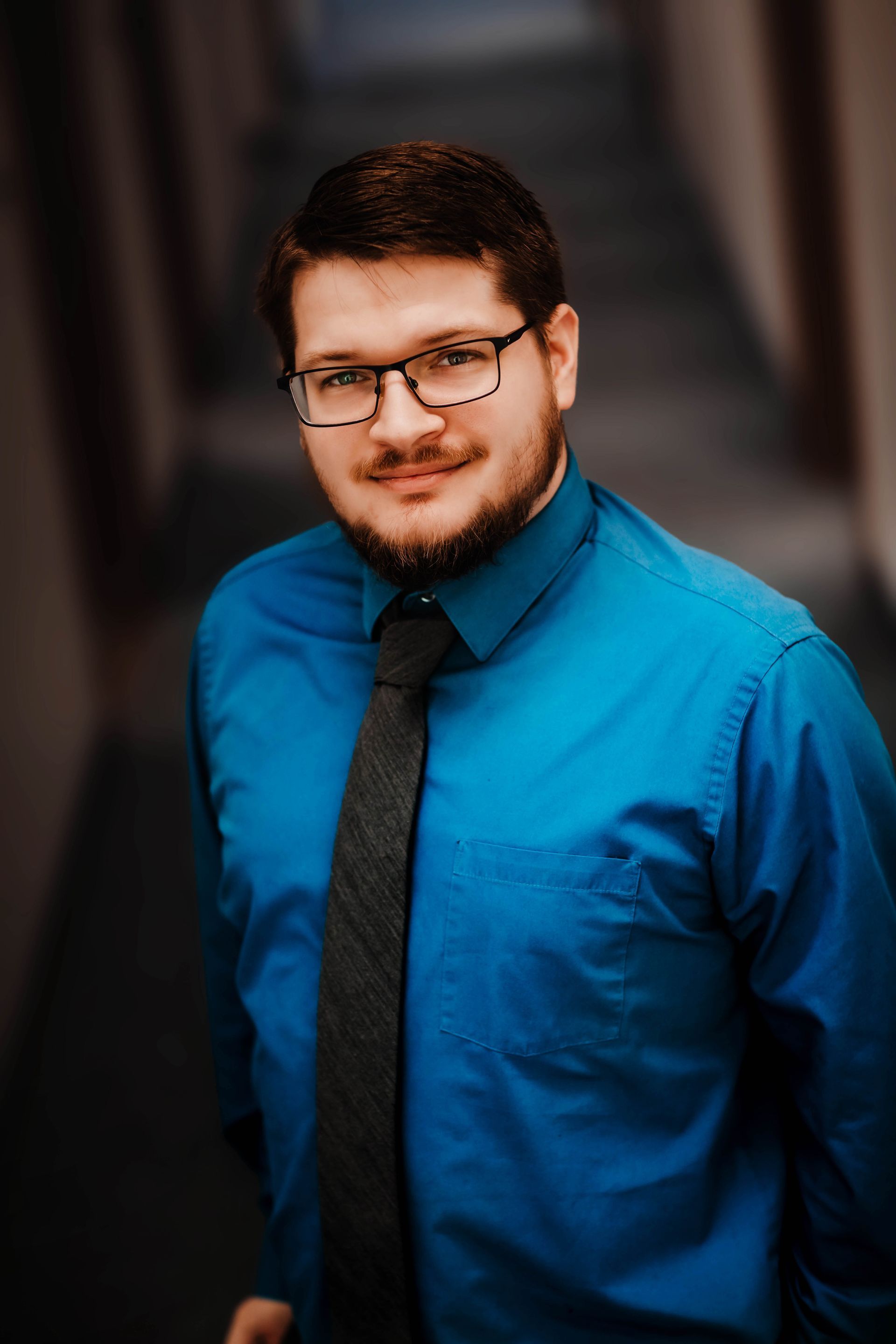 A man in a blue shirt and tie is standing in a hallway.