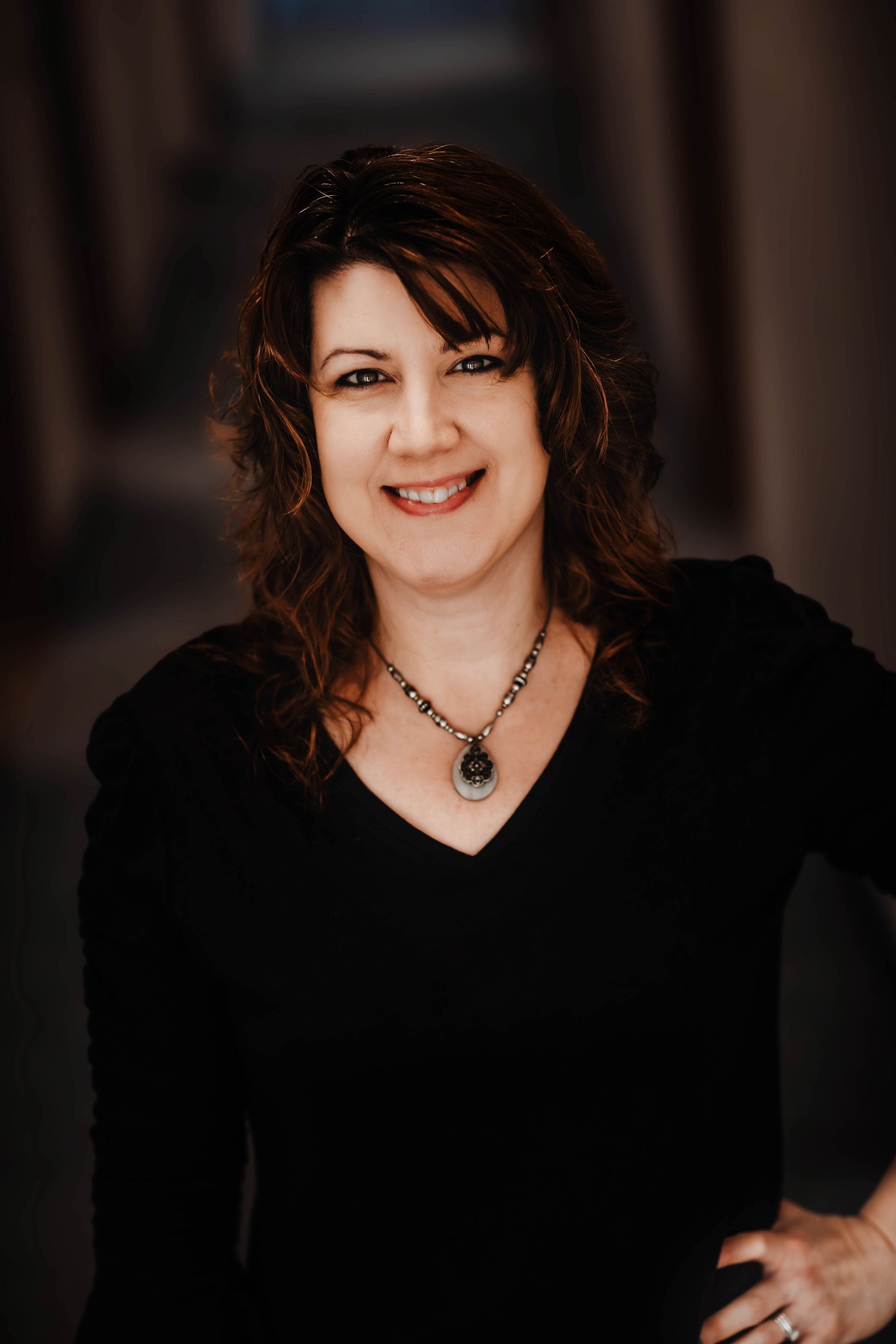 A woman wearing a black shirt and a necklace is smiling for the camera.