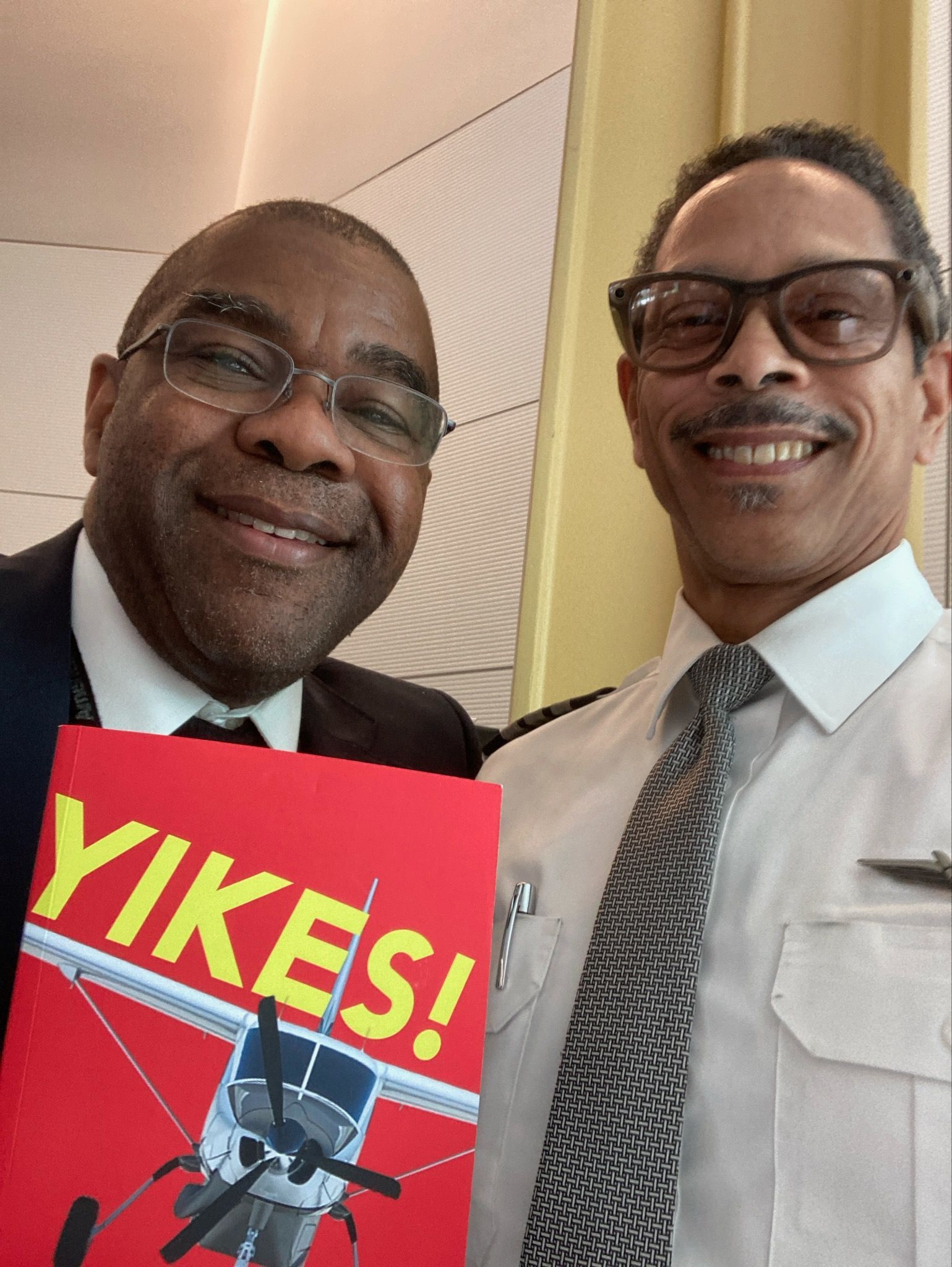 Two men are posing for a picture and one is holding a book that says yikes
