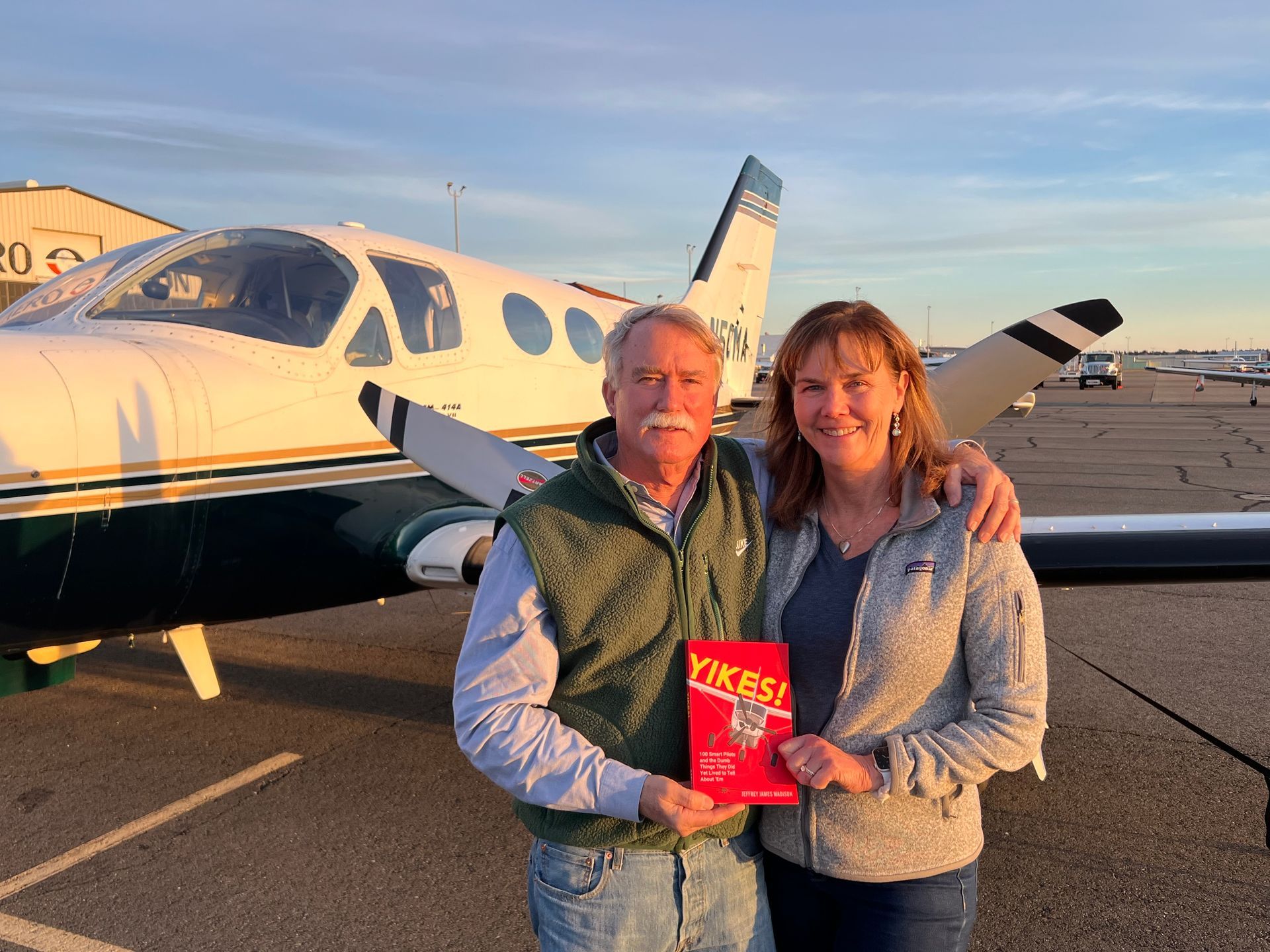 A man and a woman are standing in front of an airplane holding a book.