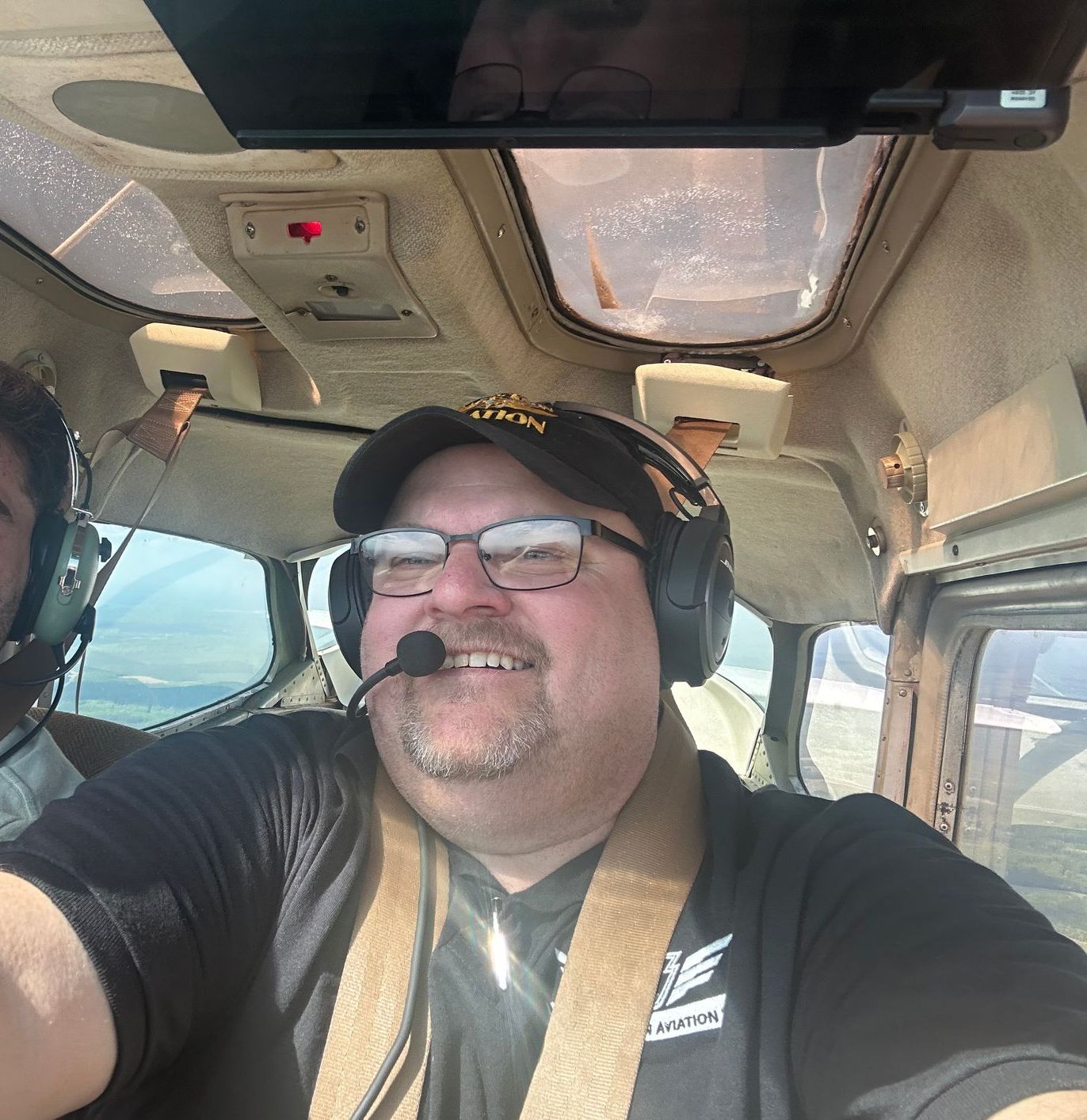 A man wearing glasses and headphones is smiling in the cockpit of an airplane