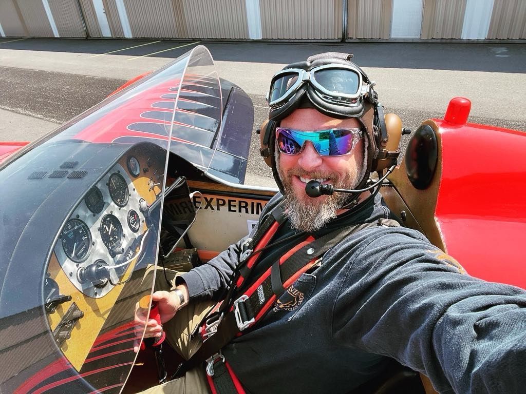 A man wearing a helmet and goggles is taking a selfie in an airplane.