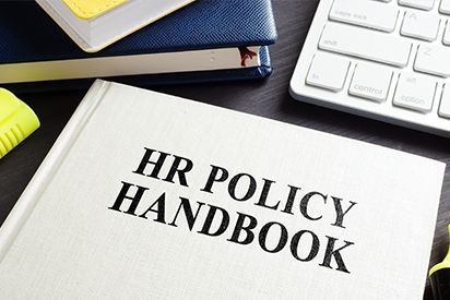 HR policy handbook on a desk with a keyboard, notebook, and highlighter.