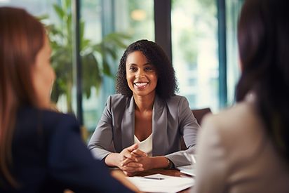 Woman in a grey blazer smiles while sitting at a table with two other women.