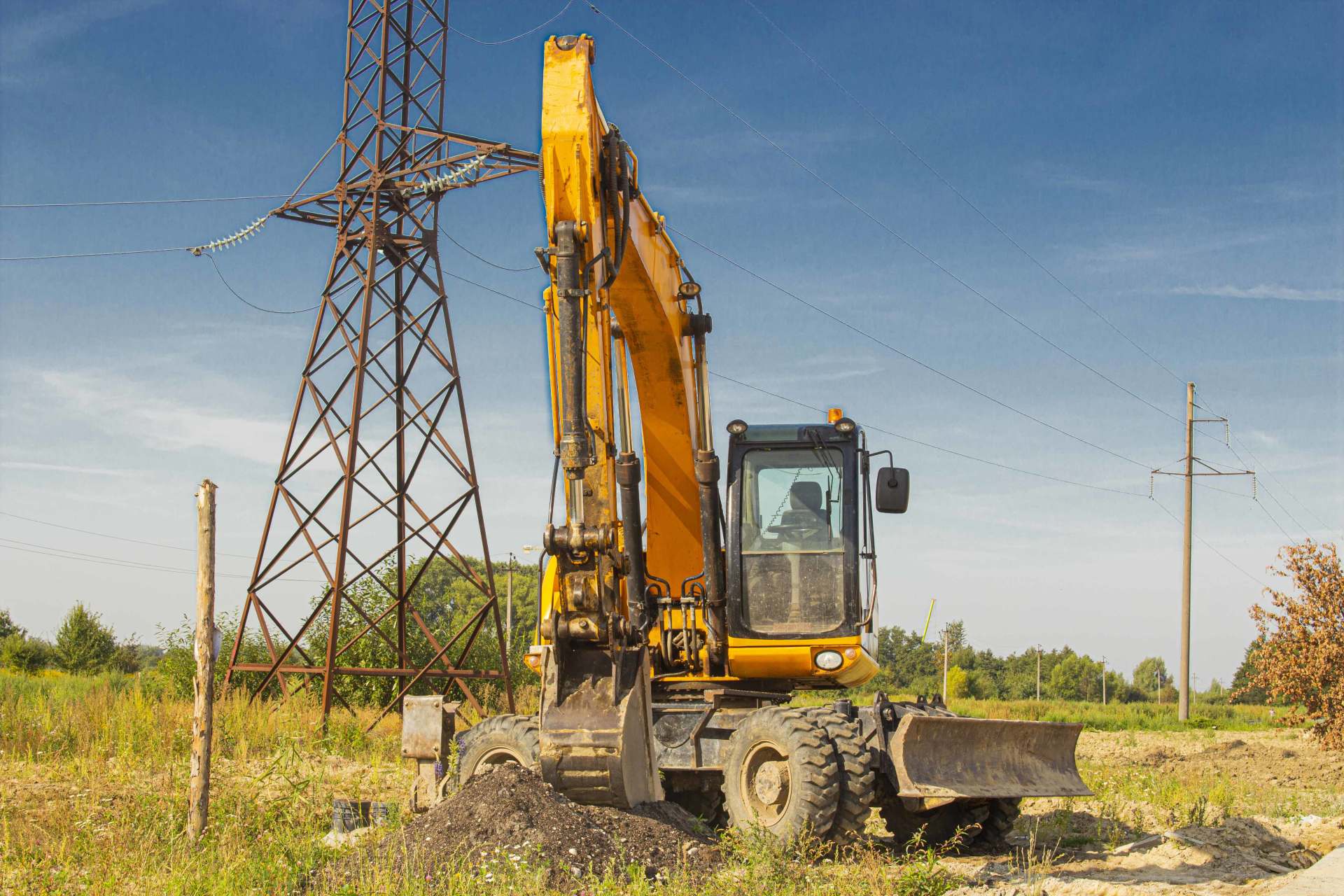 Une excavatrice jaune est assise dans un champ à côté d'une tour électrique.