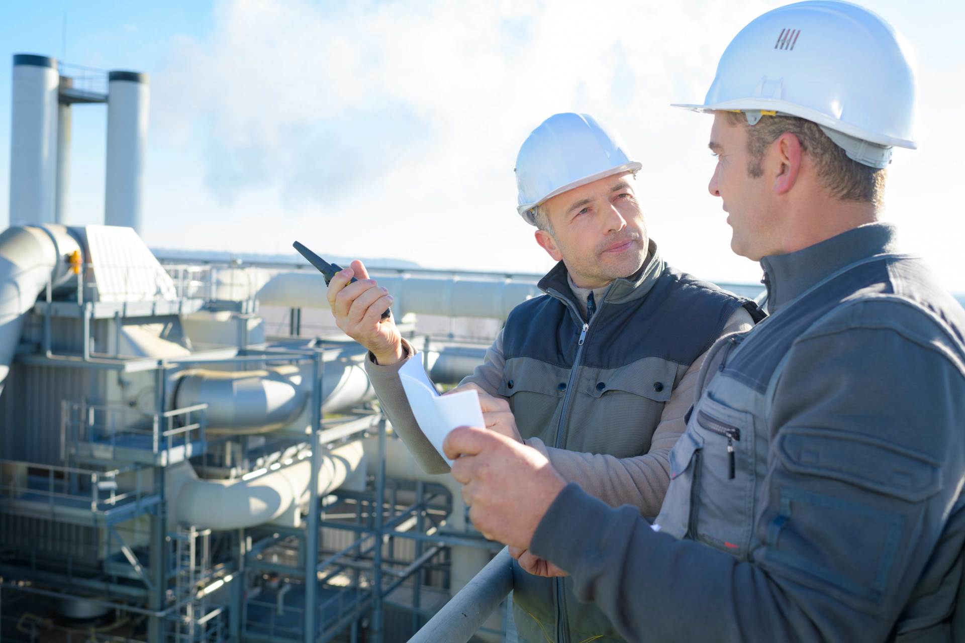 Deux hommes portant des casques de chantier se tiennent côte à côte devant une usine.