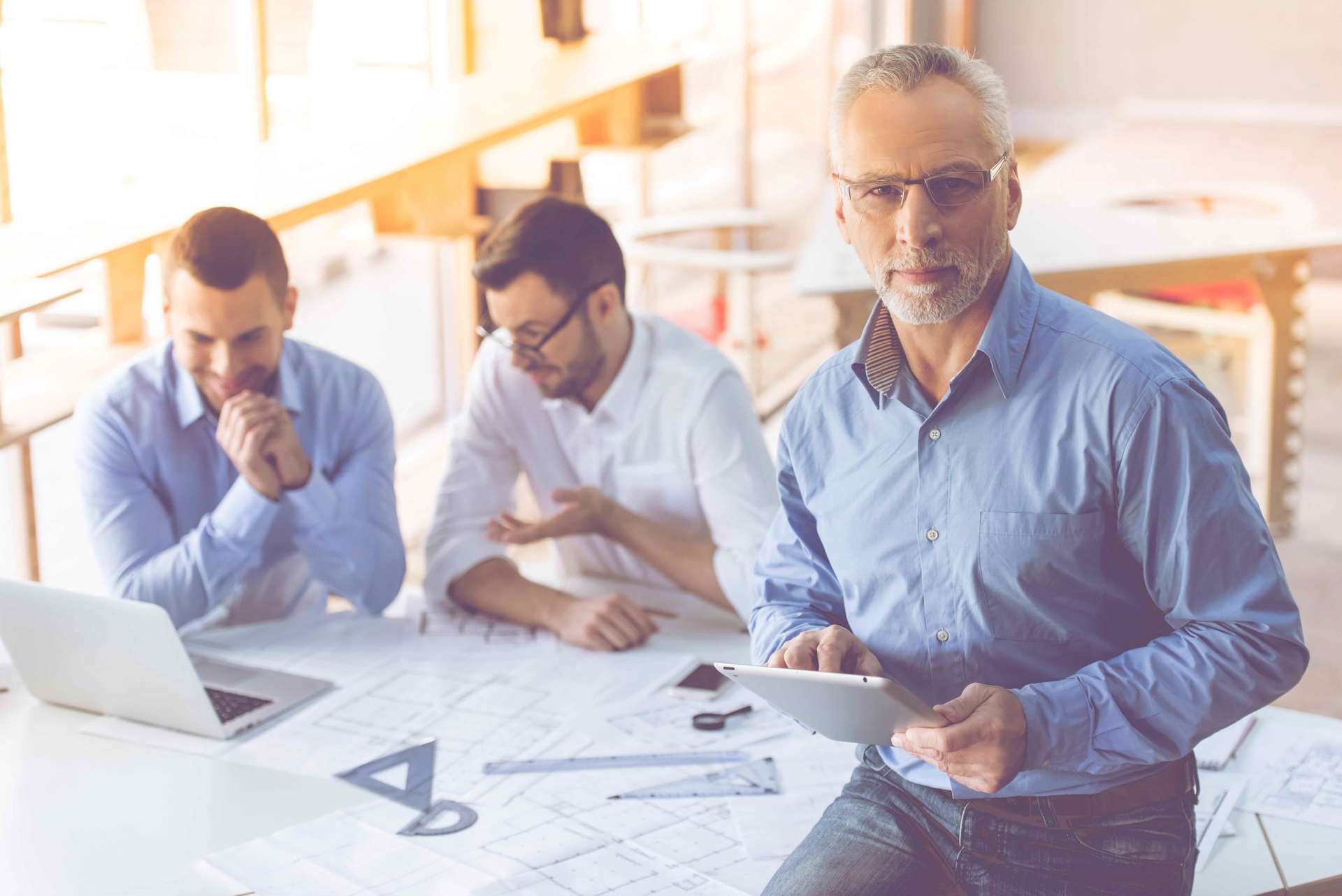 Un groupe d'hommes sont assis à une table avec un ordinateur portable et une tablette.
