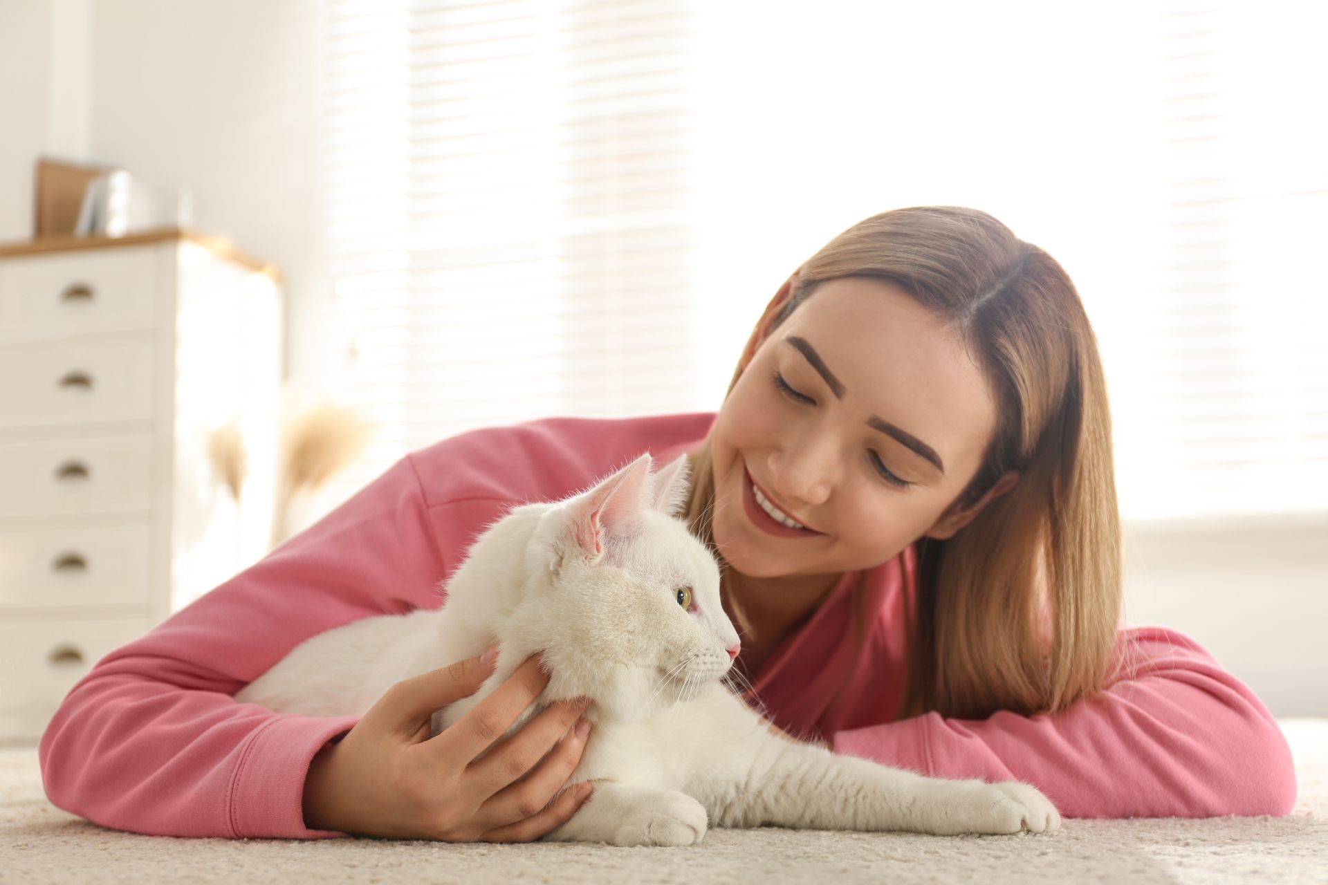 A woman is laying on the floor petting a white cat.