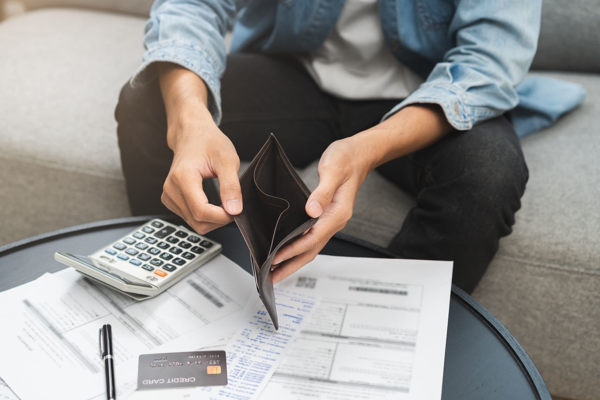 A man is sitting on a couch holding an empty wallet.