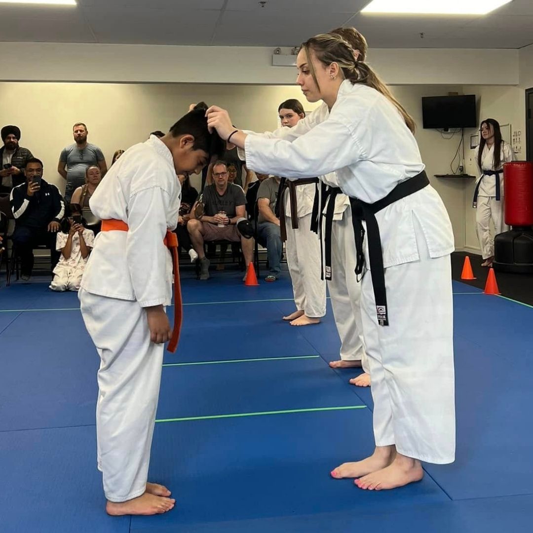 Two young children in blue and black martial arts uniforms grappling on a gym floor, one smiling.