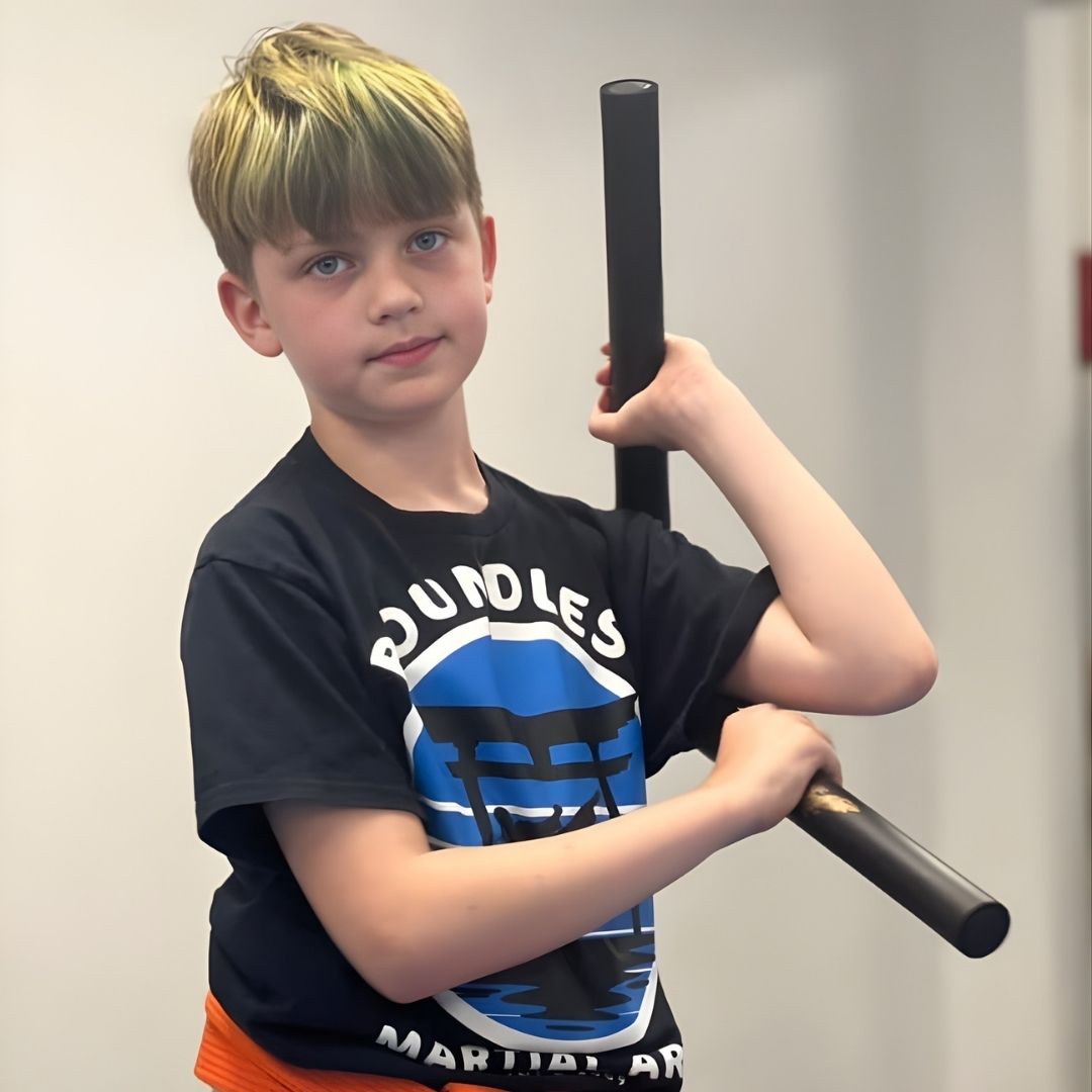 Children in colorful gis play a game on a mat. Two instructors pull a student in blue.