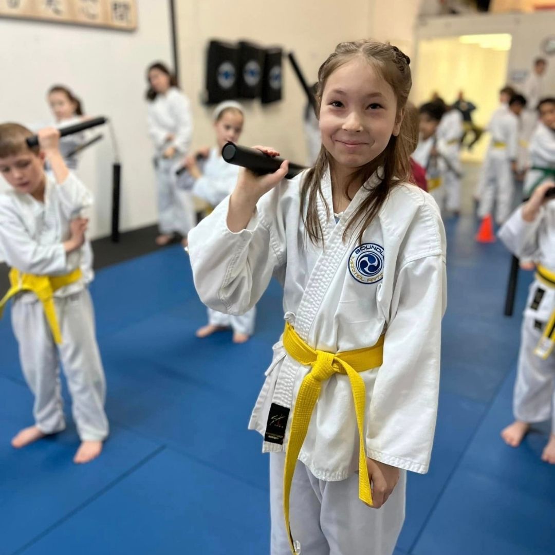 Two boys on a mat practicing Jiu-Jitsu. One boy is on top, giving a thumbs-up.