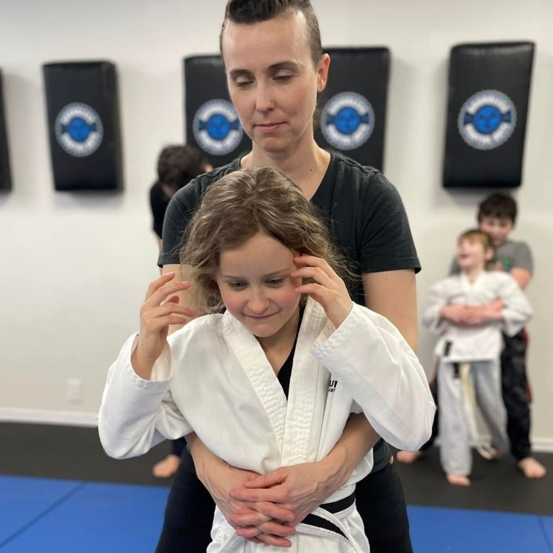 Two people grappling on a mat, one in a black gi, the other in a rash guard, legs entangled.