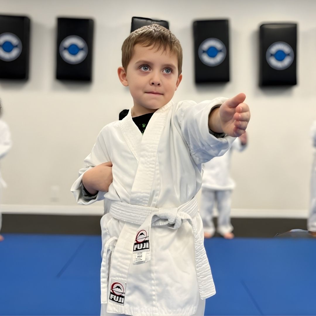 People practicing Brazilian Jiu-Jitsu. One person on the ground, another on top; two others grappling nearby. Black gis, indoor setting.